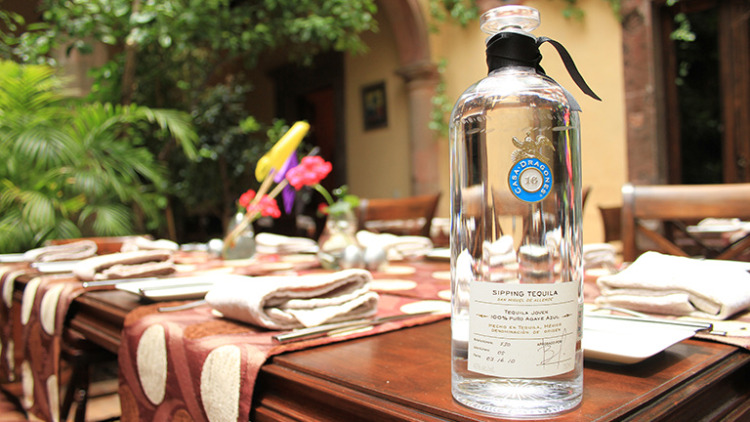 a bottle of casa dragones clear vodka sitting on a wood table outside