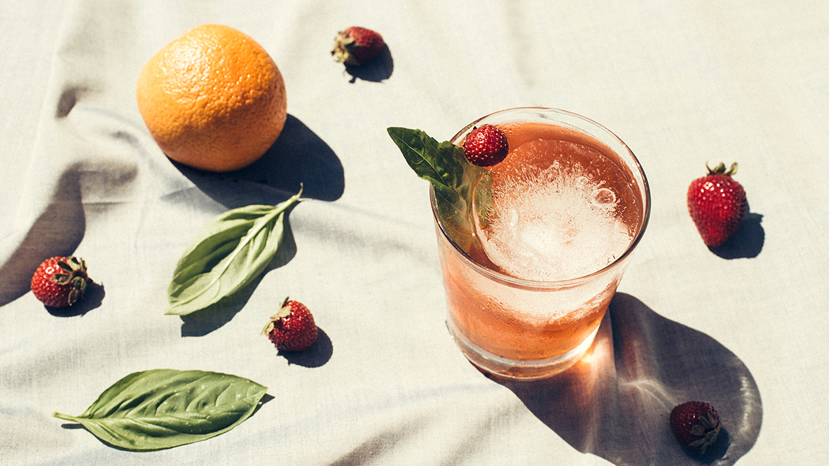 A cocktail placed on a white table cloth adorned with oranges and strawberries