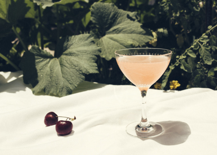 pink cocktail on an outdoor table next to cherries