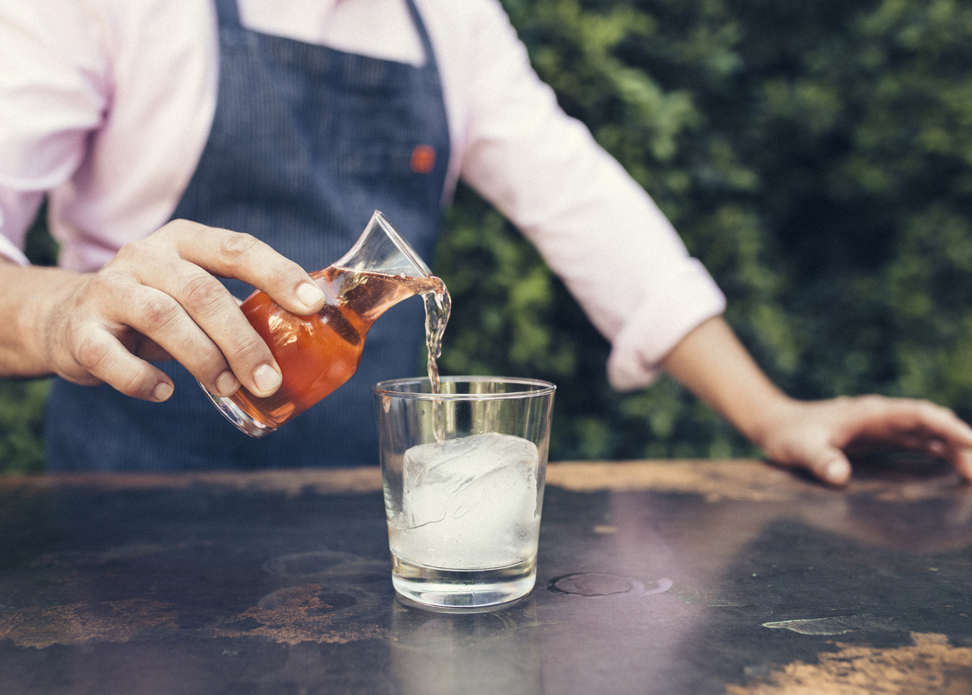 bartender pouring drink from carafe into glass with large square ice cube