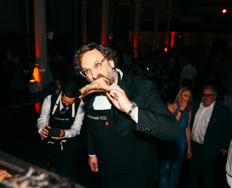 man in dark room wearing a beefsteak 8 apron while eating a large piece of steak