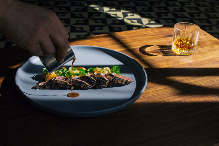 chef pouring sauce onto plate with steak