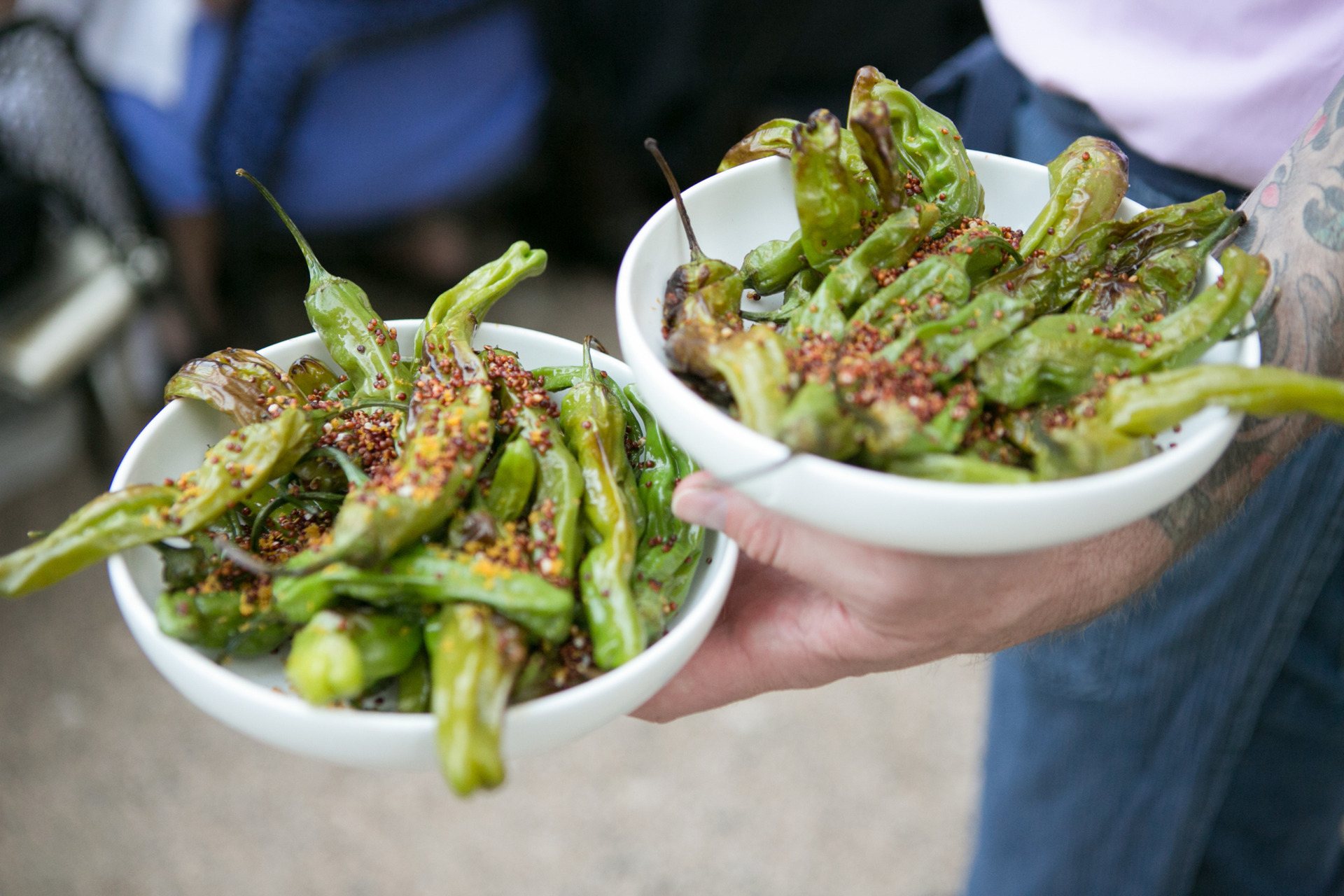 waiter holding two white bowls filled with shishito peppers