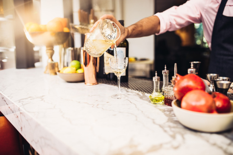 bartender pouring yellow cocktail with pink shirt and blue apron