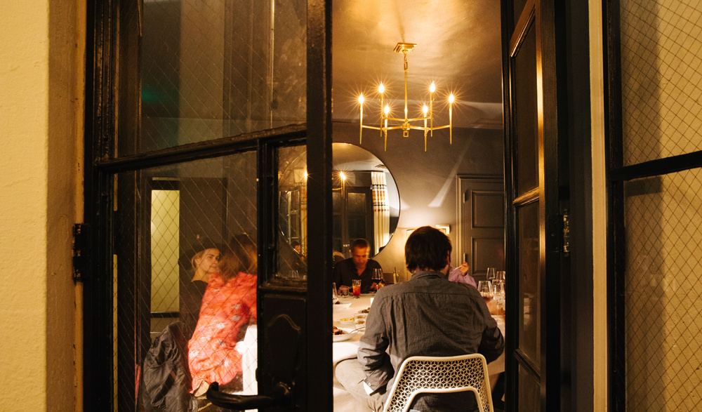 Outside looking in view of people at dinner table sitting on white mesh chairs.