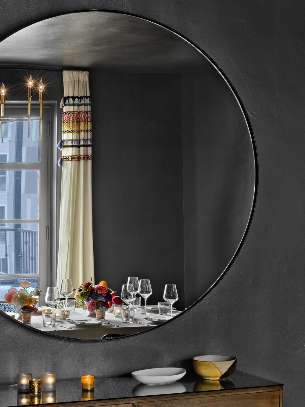 mirror reflection of room with set table and wooden credenza