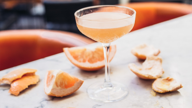 Forbidden Cocktail in orange with orange peels and barstools surrounding