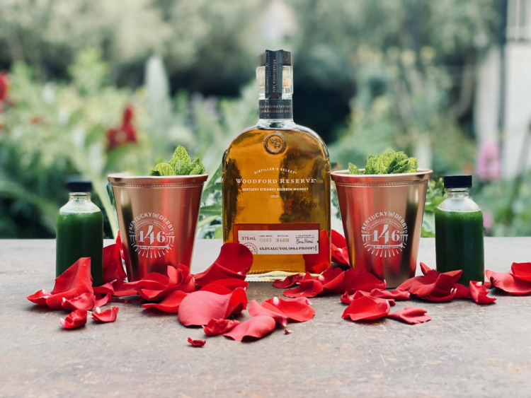 Bottle of bourbon with copper cups and rose petals on a table for Kentucky derby