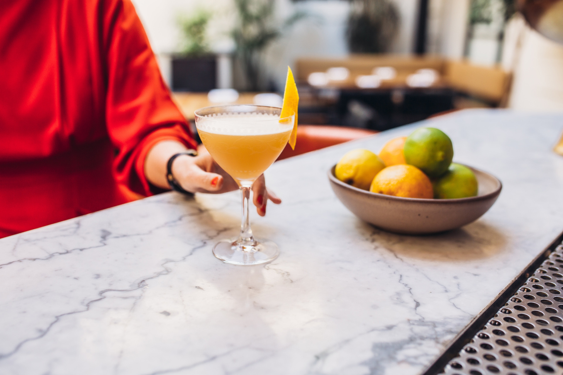 woman in red dress holding cocktail with lemon peel on top at bar in coup glass