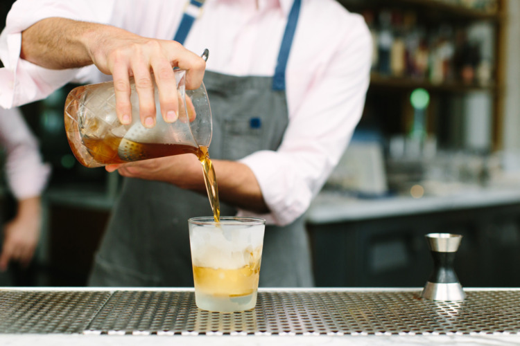 bartender pouring dark spirit out of a mixing glass