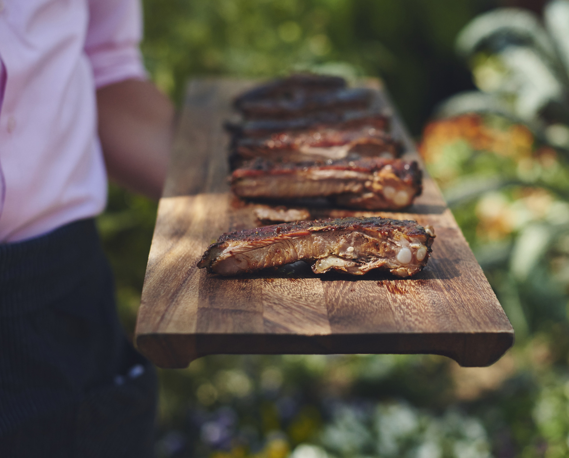 man in pink shirt holding ribs cut on a board in a garden