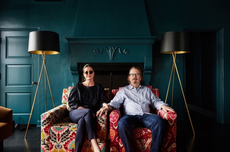 photo of Amy and neal fraser on a colorful couch with teal walls wearing glasses