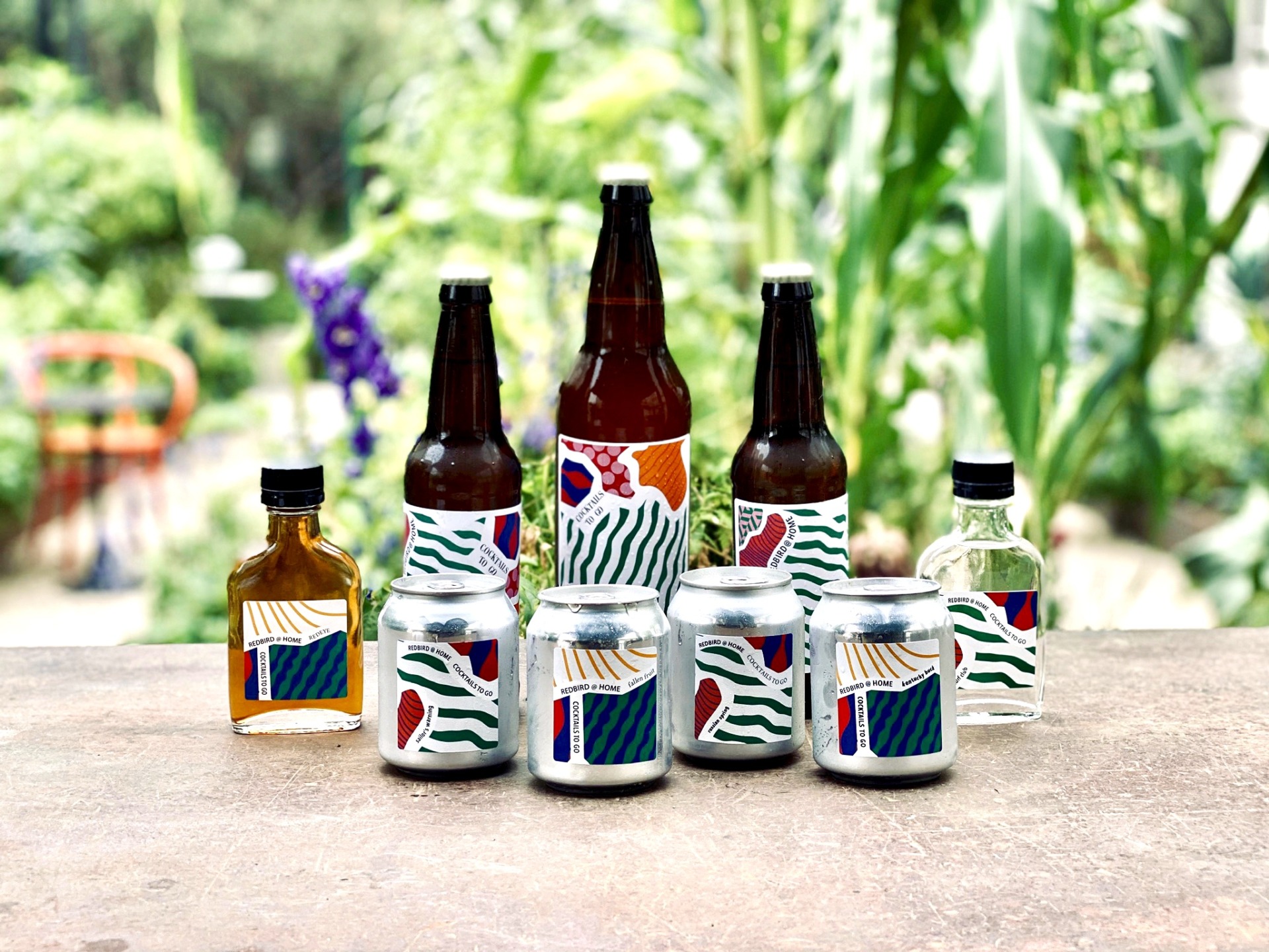 bottled of cocktails with funky labels sitting on a table with garden in background