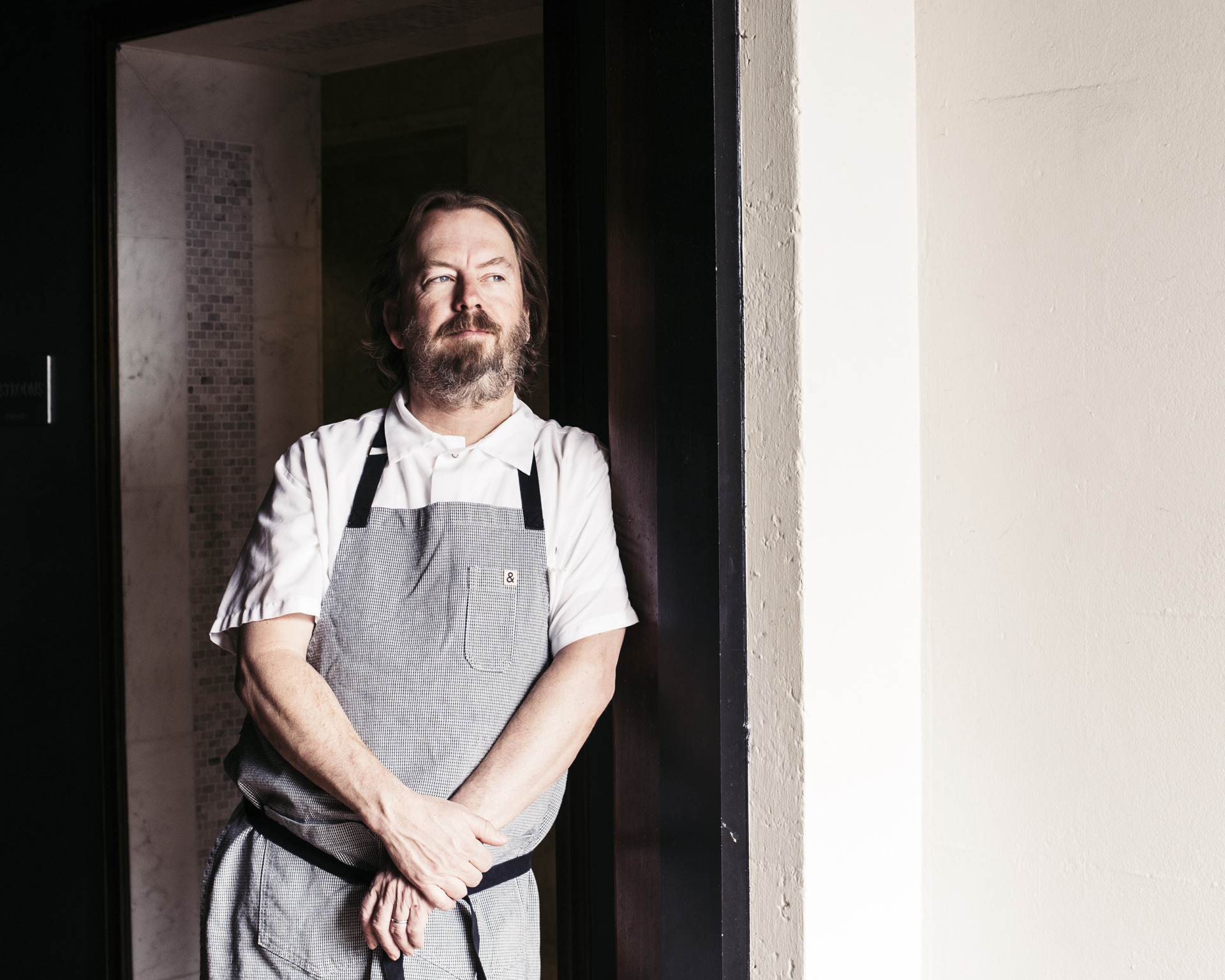 Neal Fraser leaning against wall in grey apron