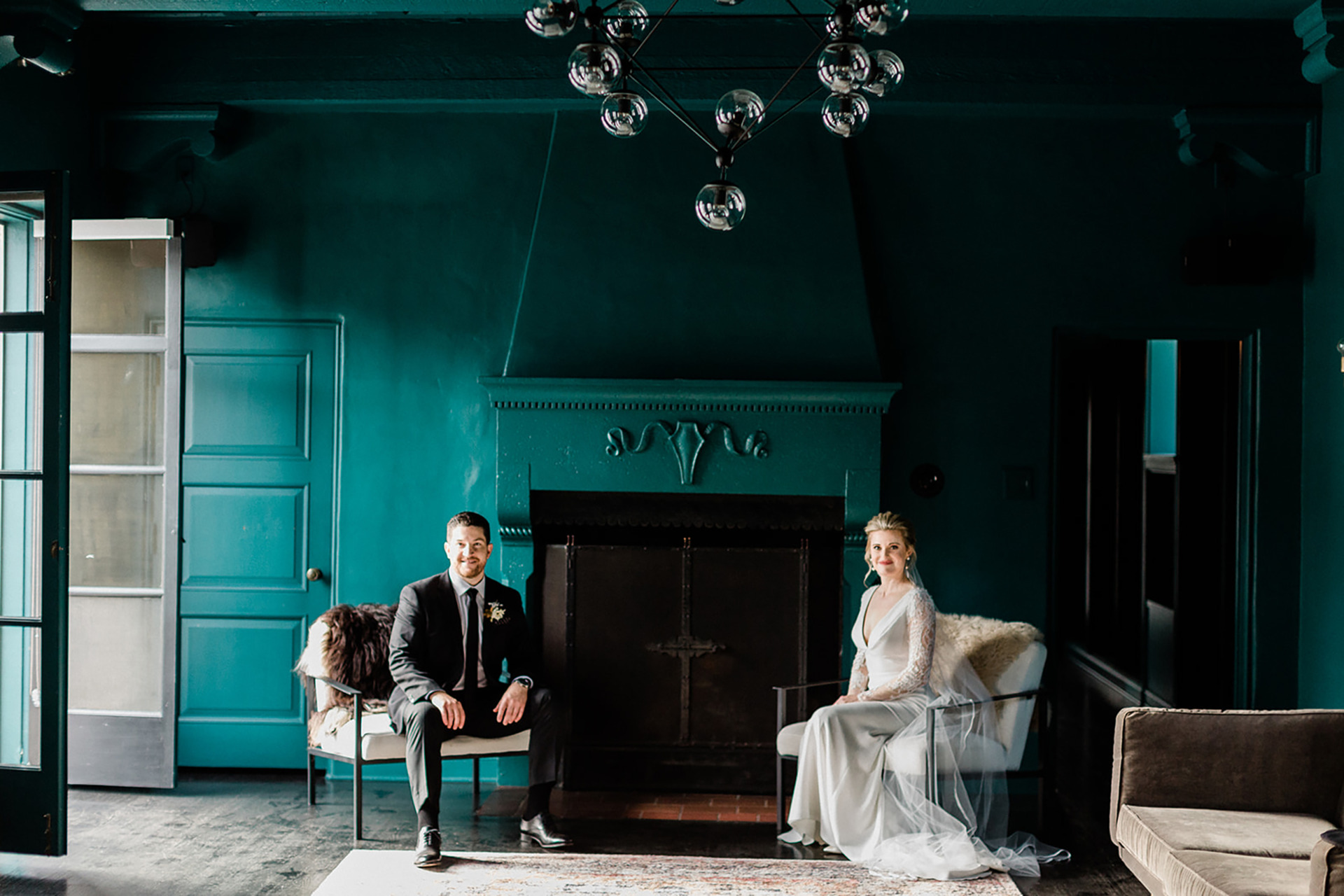 bride and groom sitting on white chairs in room with green walls