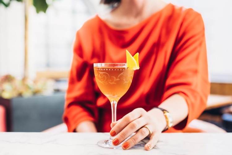 woman with orange nails and dress holding an orange cocktail