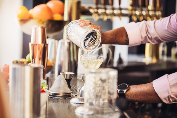 bartender pouring a cocktail into a glass