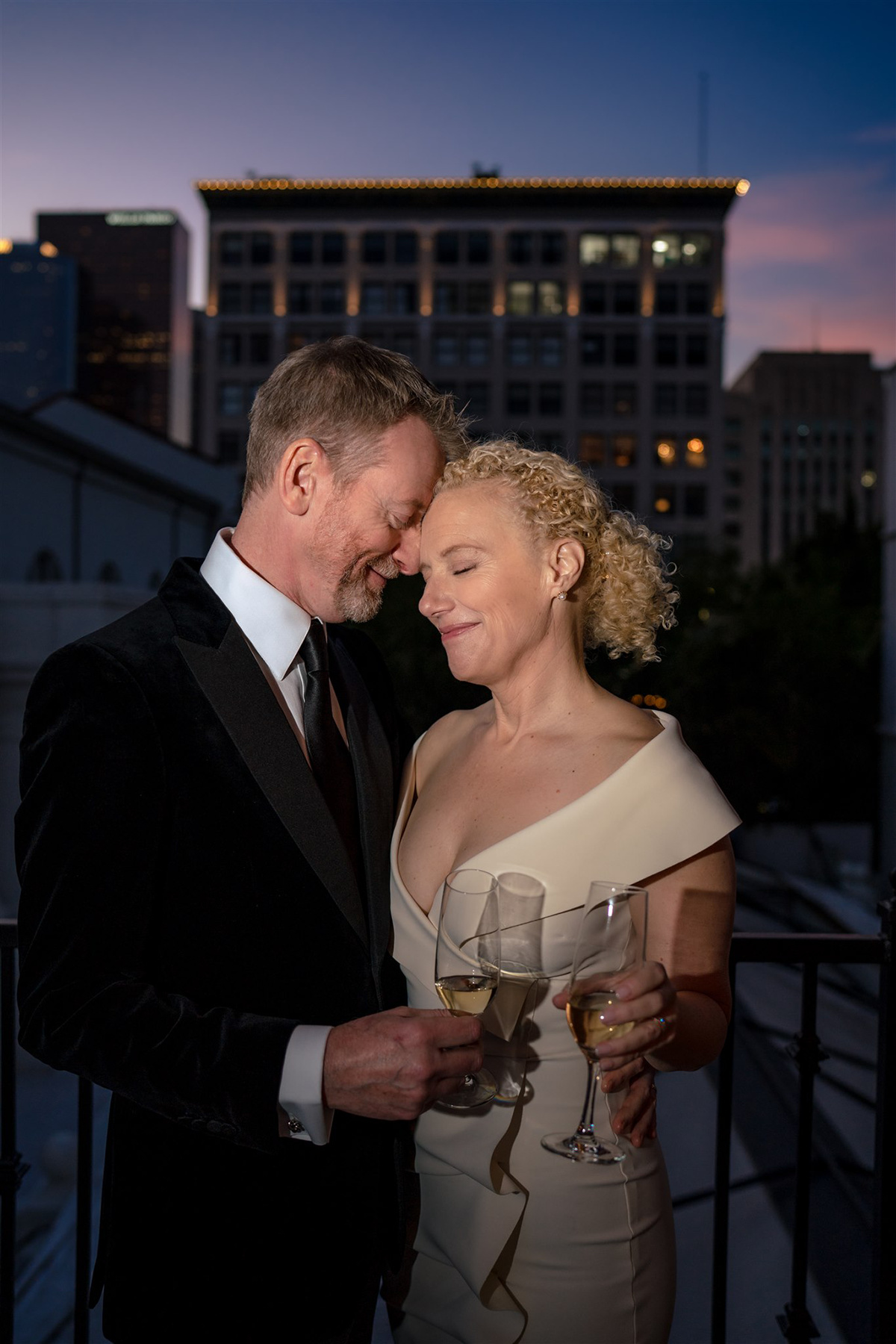 a bride and groom sharing an intimate moment on outdoor patio in front of skyline holding champagne