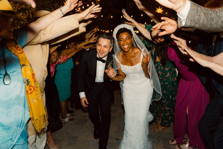 a bride and groom make their way through a tunnel made by guests raising their arms