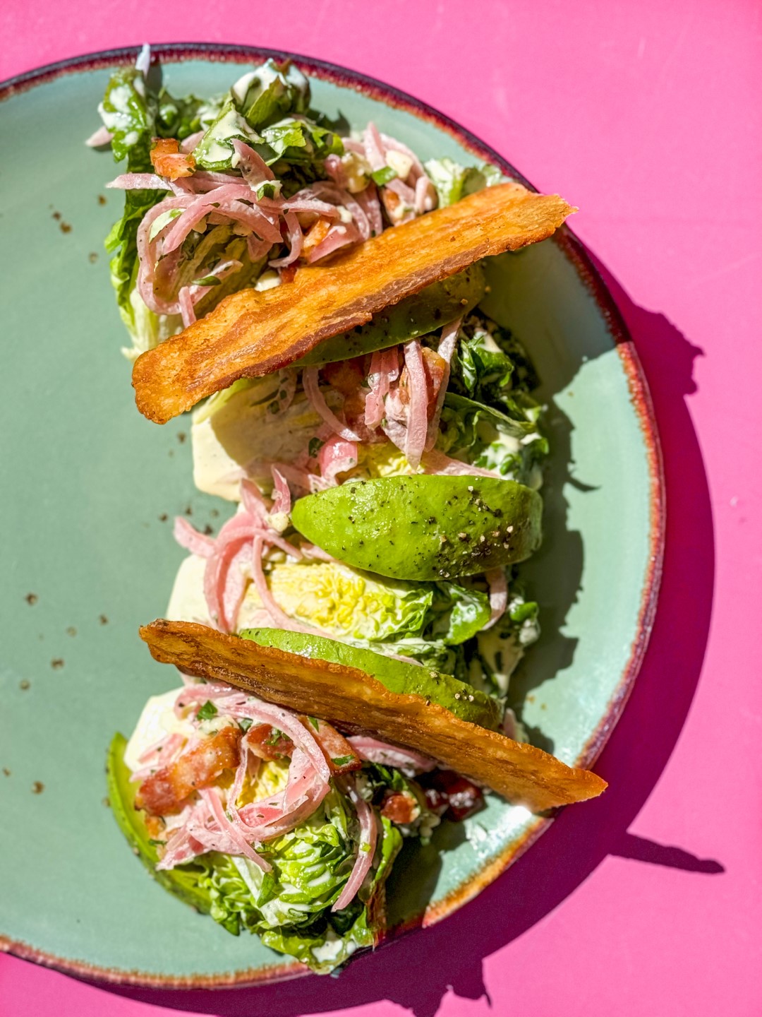 avocado salad on a teal plate with a pink background