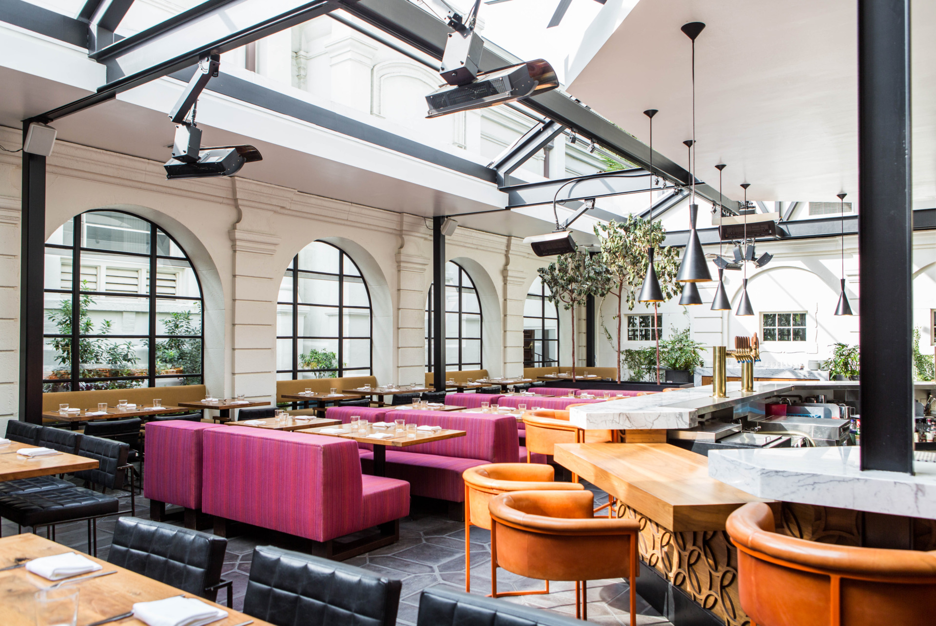 the Redbird Main Dining Room with tables set for dinner service, pink booths, orange bar stools