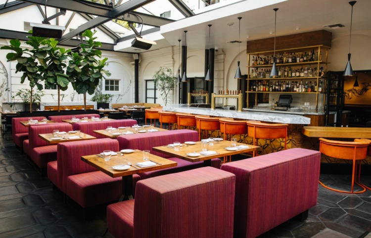 Redbird's Main Dining Room with plush pink banquette chairs and a wraparound bar with orange stools