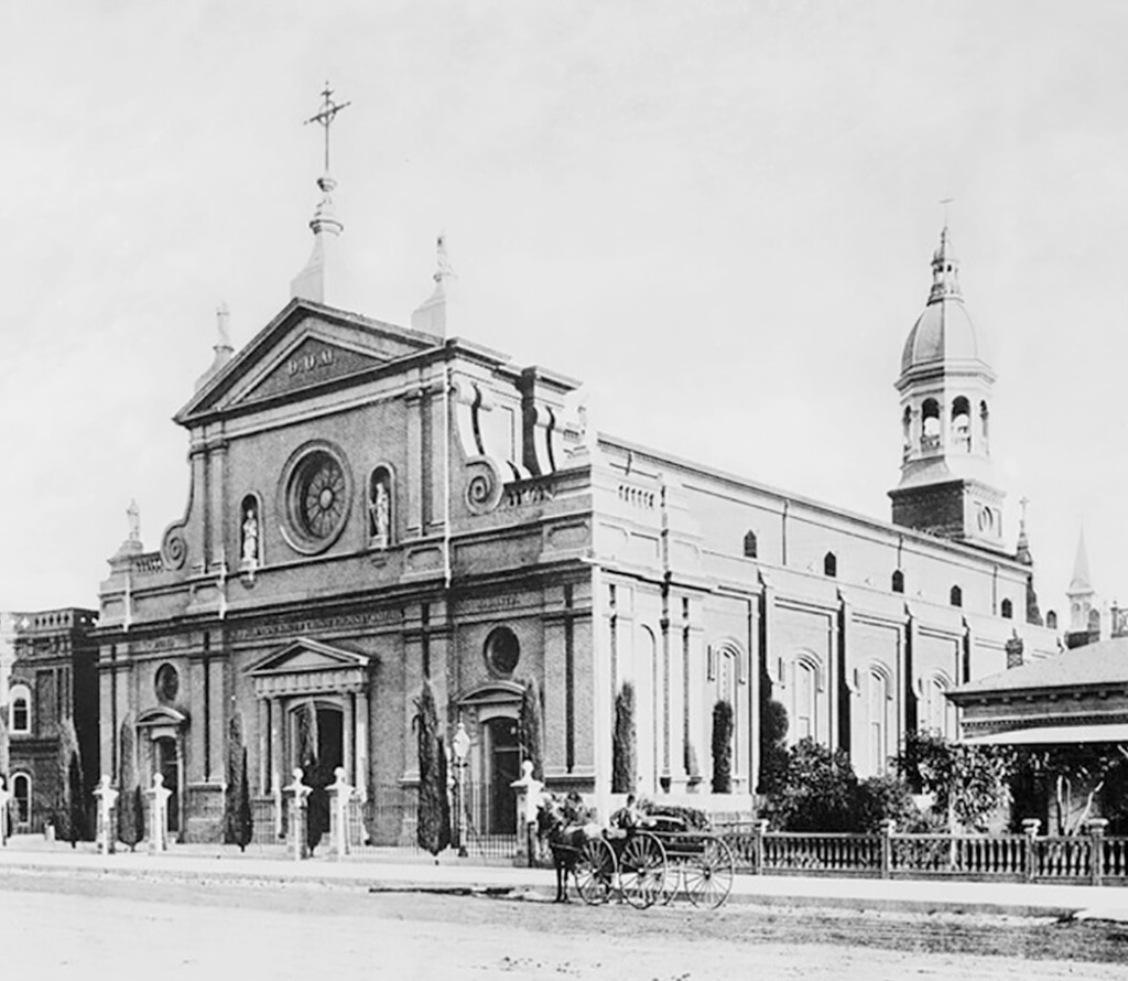 an archival black and white photo of St Vibiana in the 1800s with a horse and buggy out front