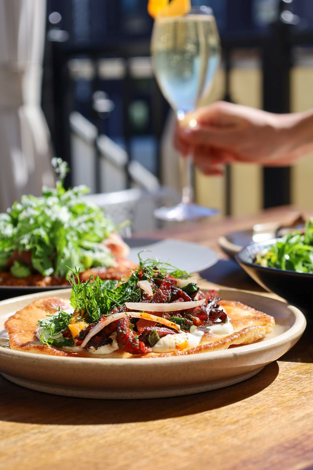 Flatbread with a yogurt sauce, meat, and herbs on top.