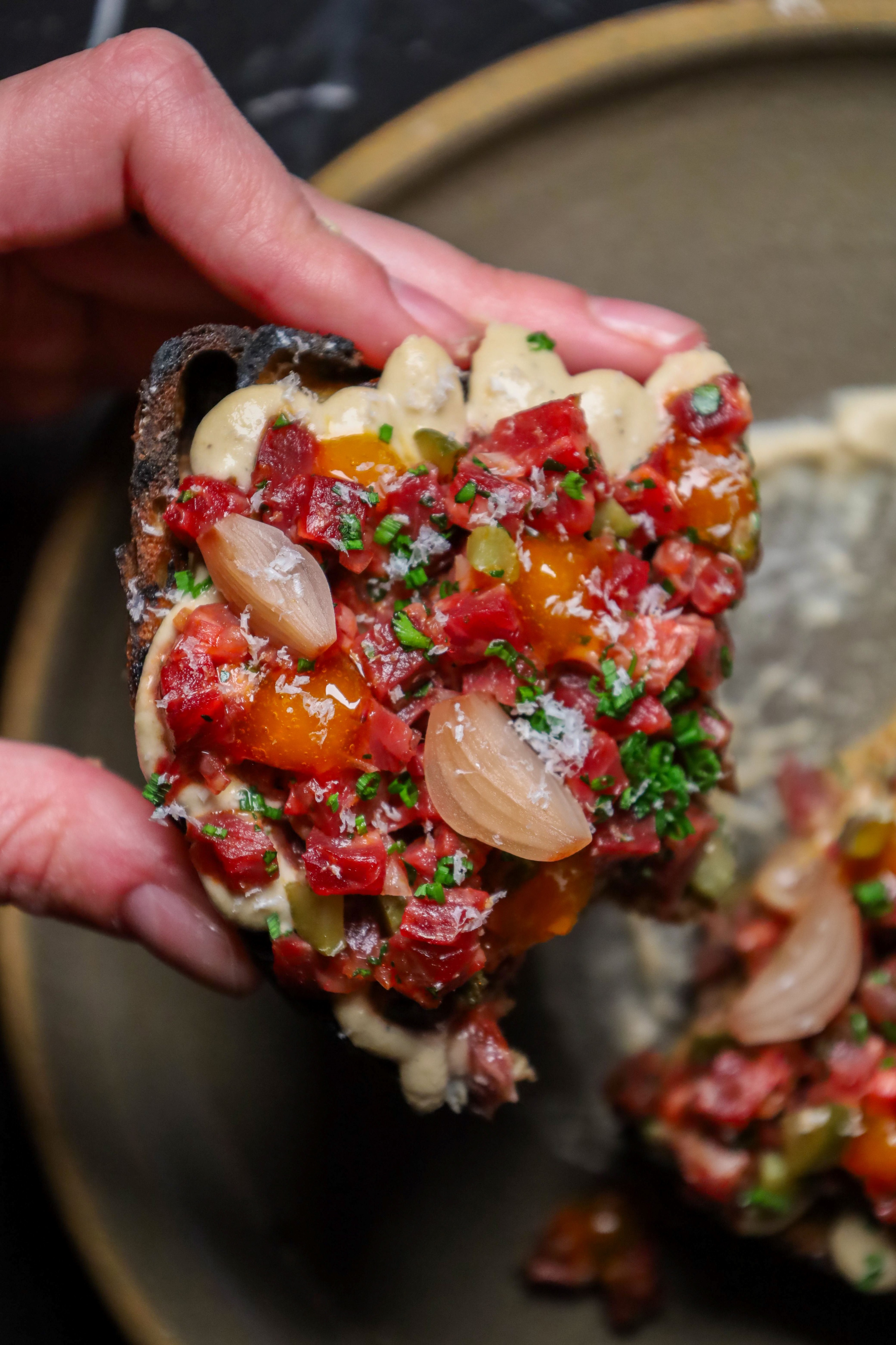 hand holding toast with aioli and chopped beef tartare