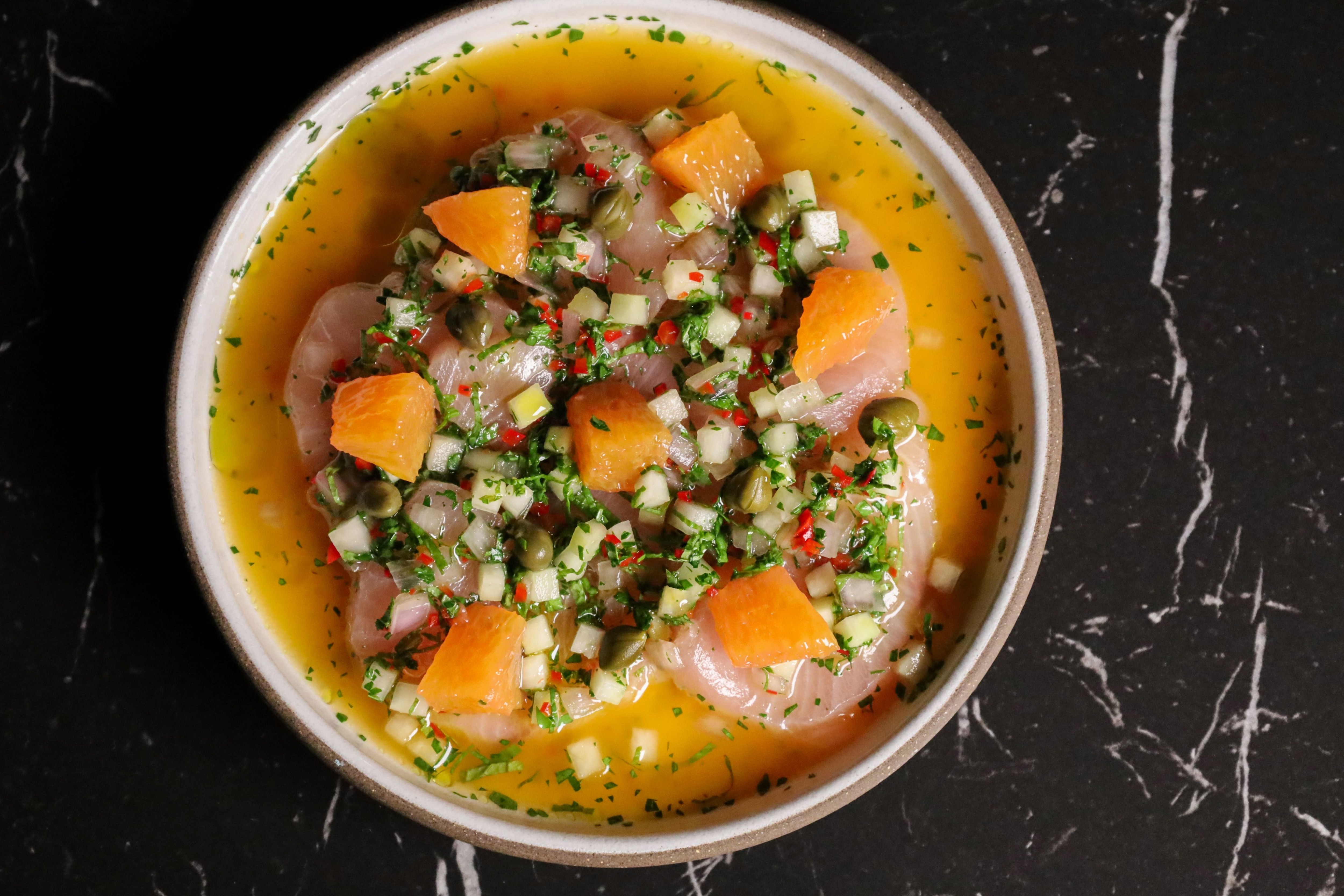 raw fish topped with orange segments, capers, shallot, and olive oil on a plate