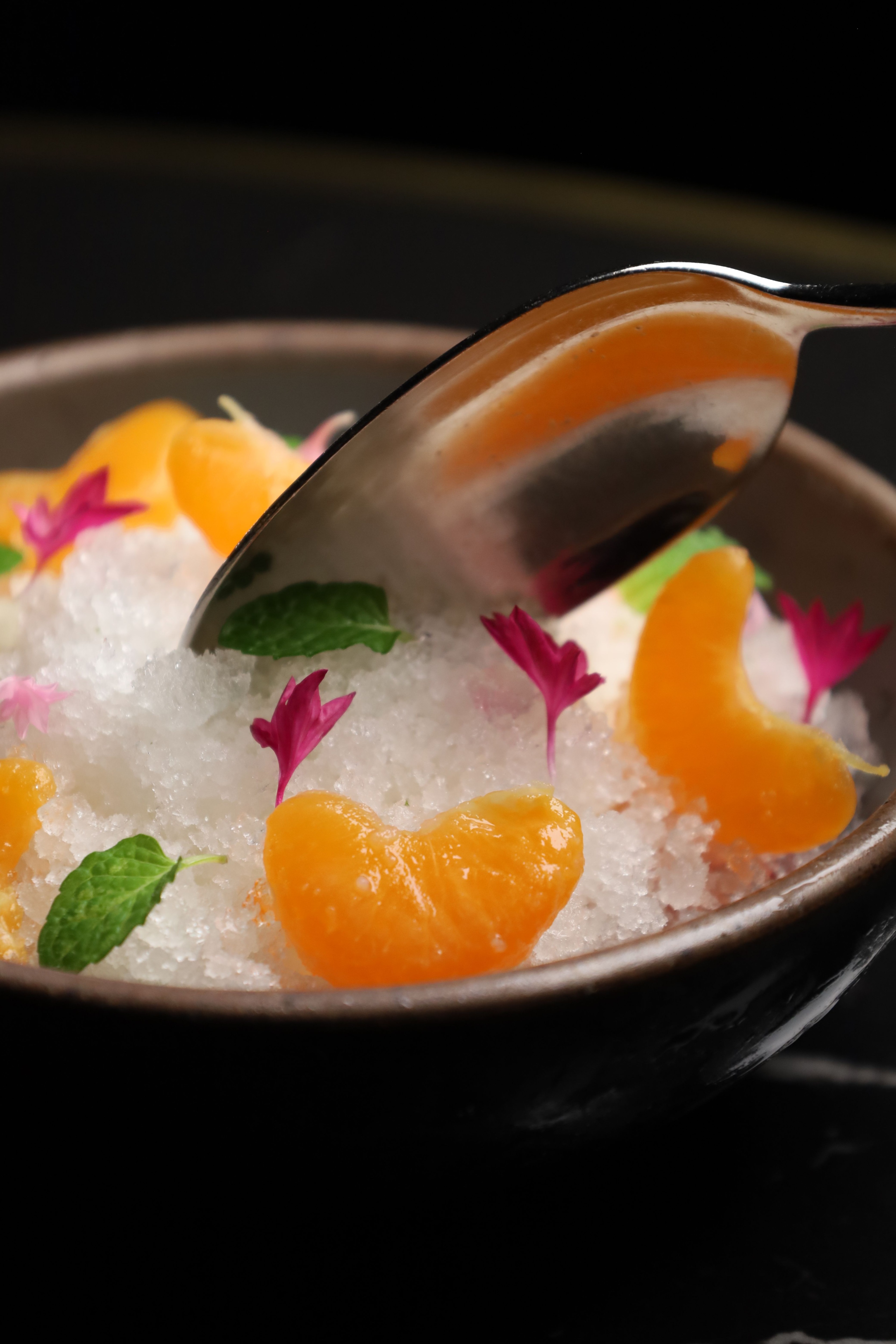 a spoon dipping into a bowl of granite with tangerine segments