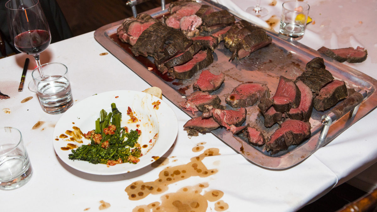 large platter of rare steak on a messy table
