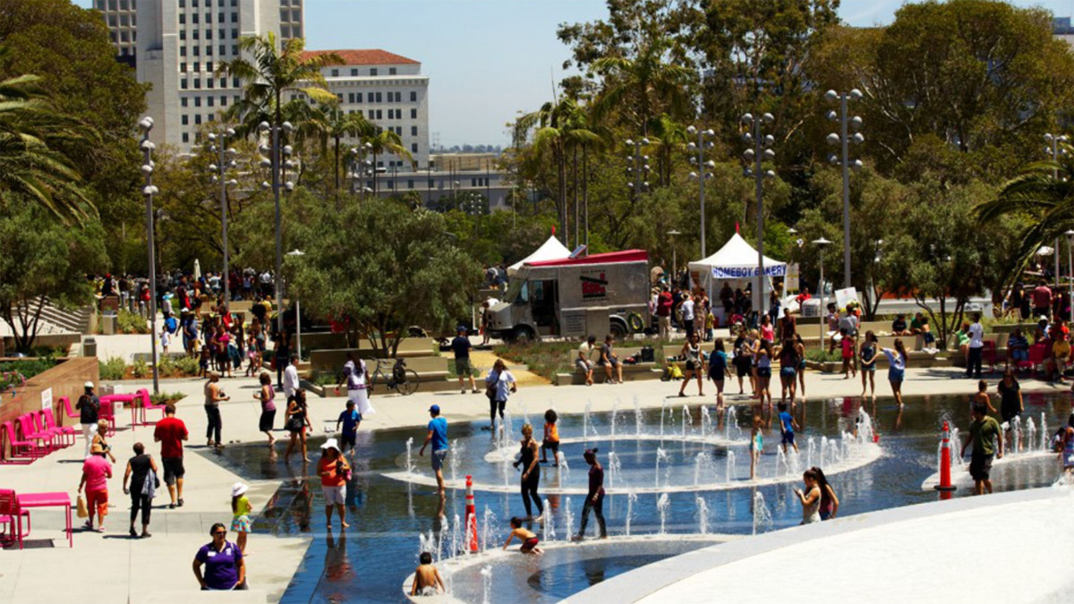 public park on a sunny day filled with people walking through water fountains