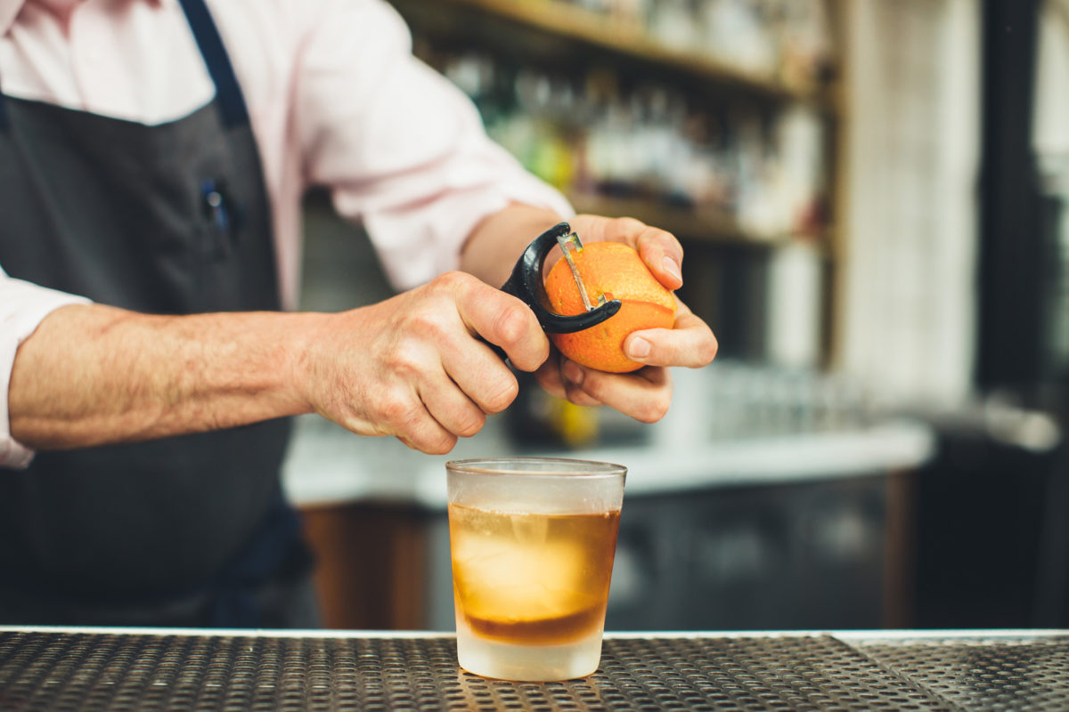 bartender peeling an orange over a cocktail