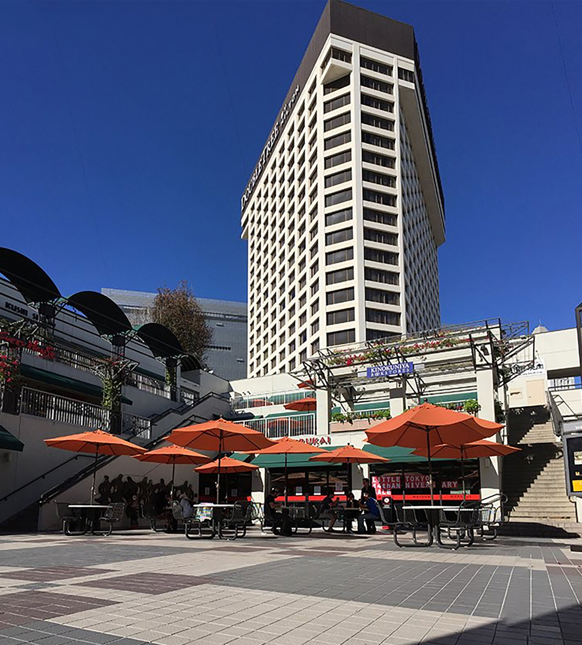 tall white building with patio filled with tables and orange umbrellas on a sunny day