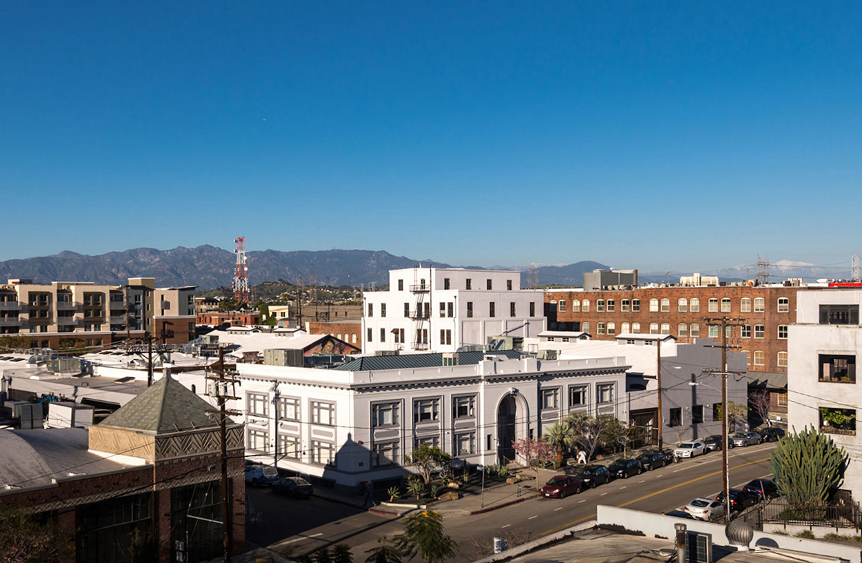 View of buildings surrounded by Los Angeles mountains on a sunny day, with a large white building being the most prominant
