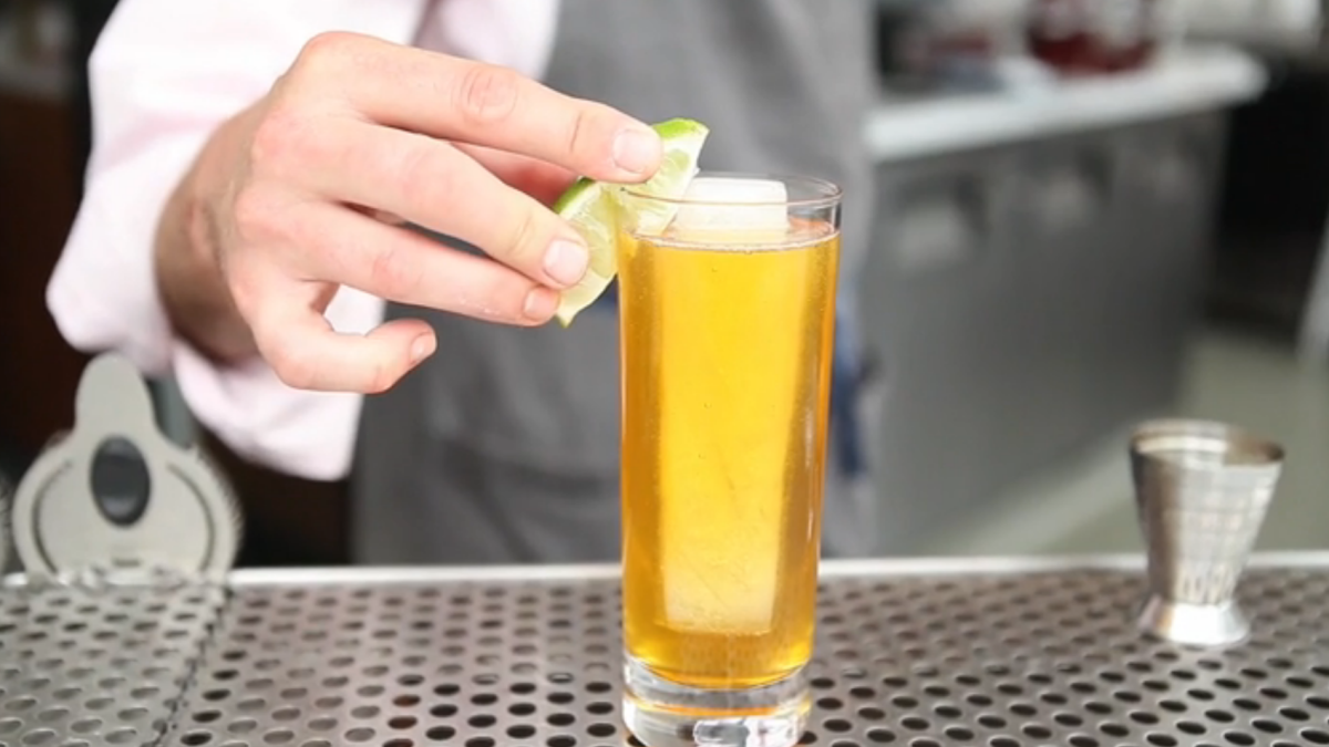 bartender adding lime slice to cocktail that has a long piece of ice