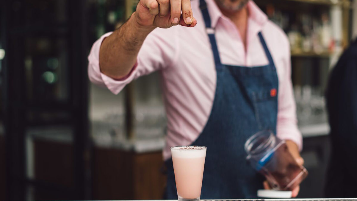 Bartender sprinkling spice into a pink cocktail