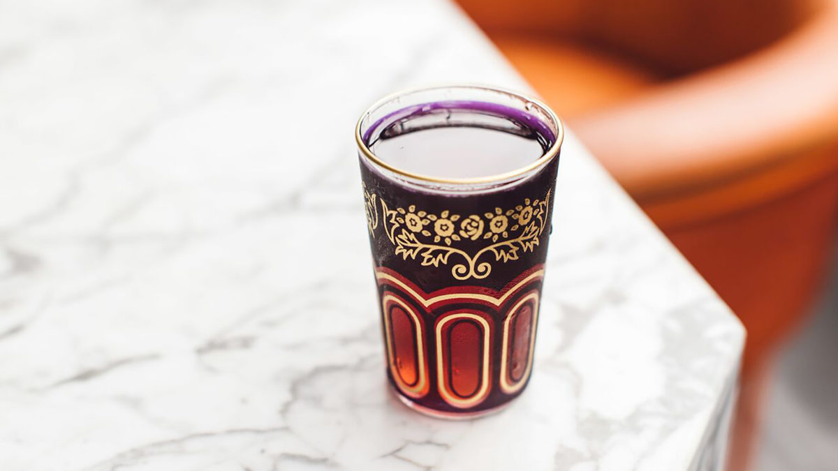 A purple cocktail in a glass featuring a gold rim and patterns