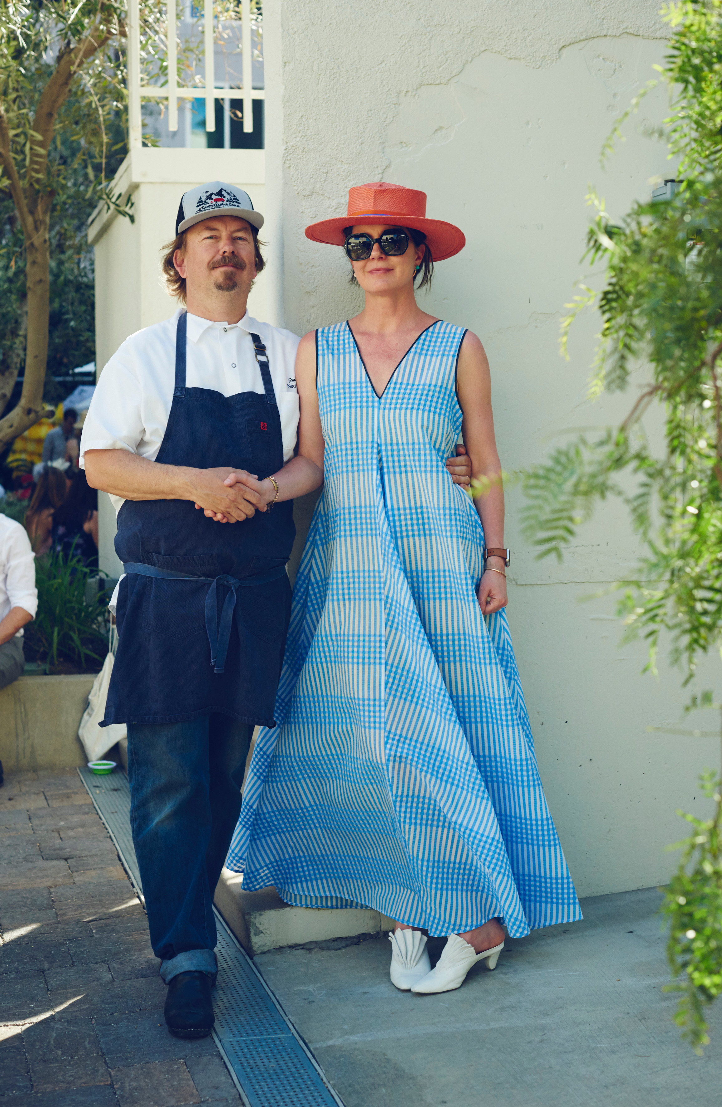 Amy Knoll Fraser in blue dress and red hat holding hands with chef in apron