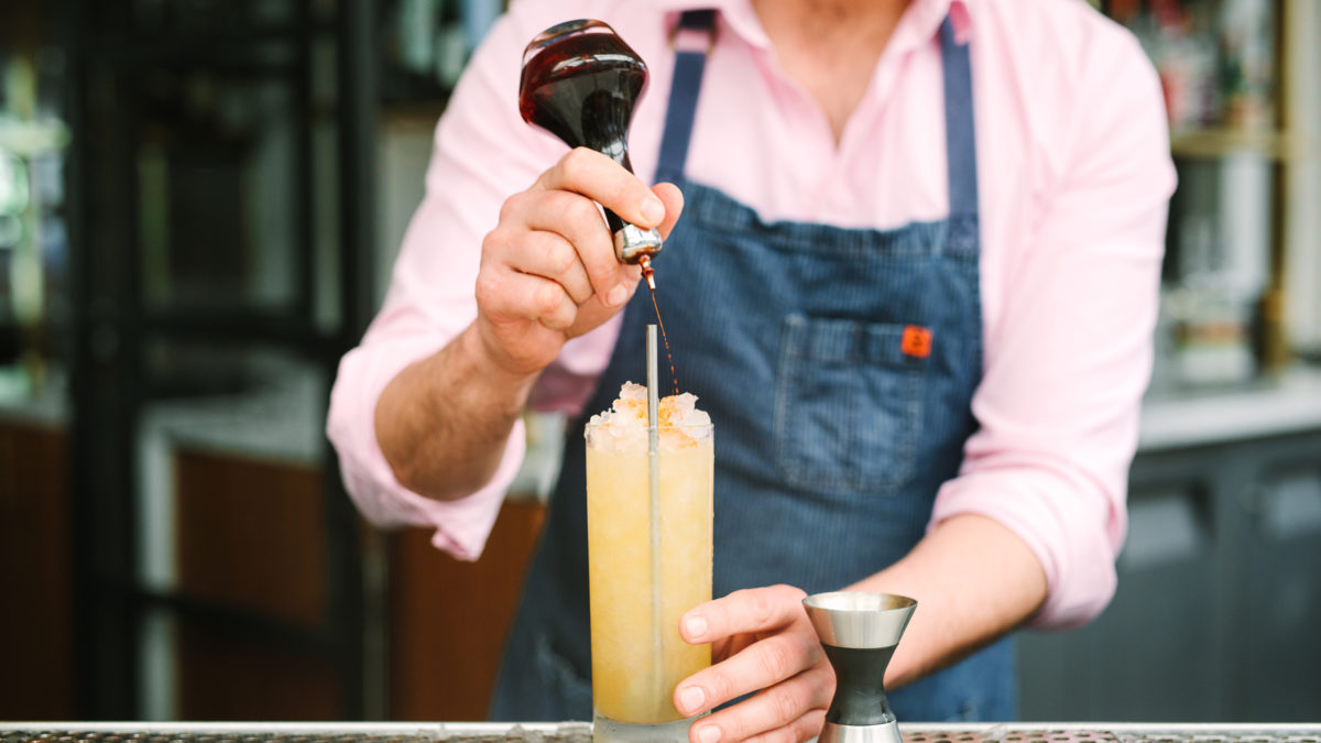 bartender pouring a syrup into a black-eyed susan cocktail