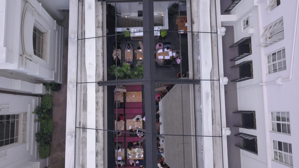 birds eye viewing looking down from outside at glass ceiling with diners eating inside