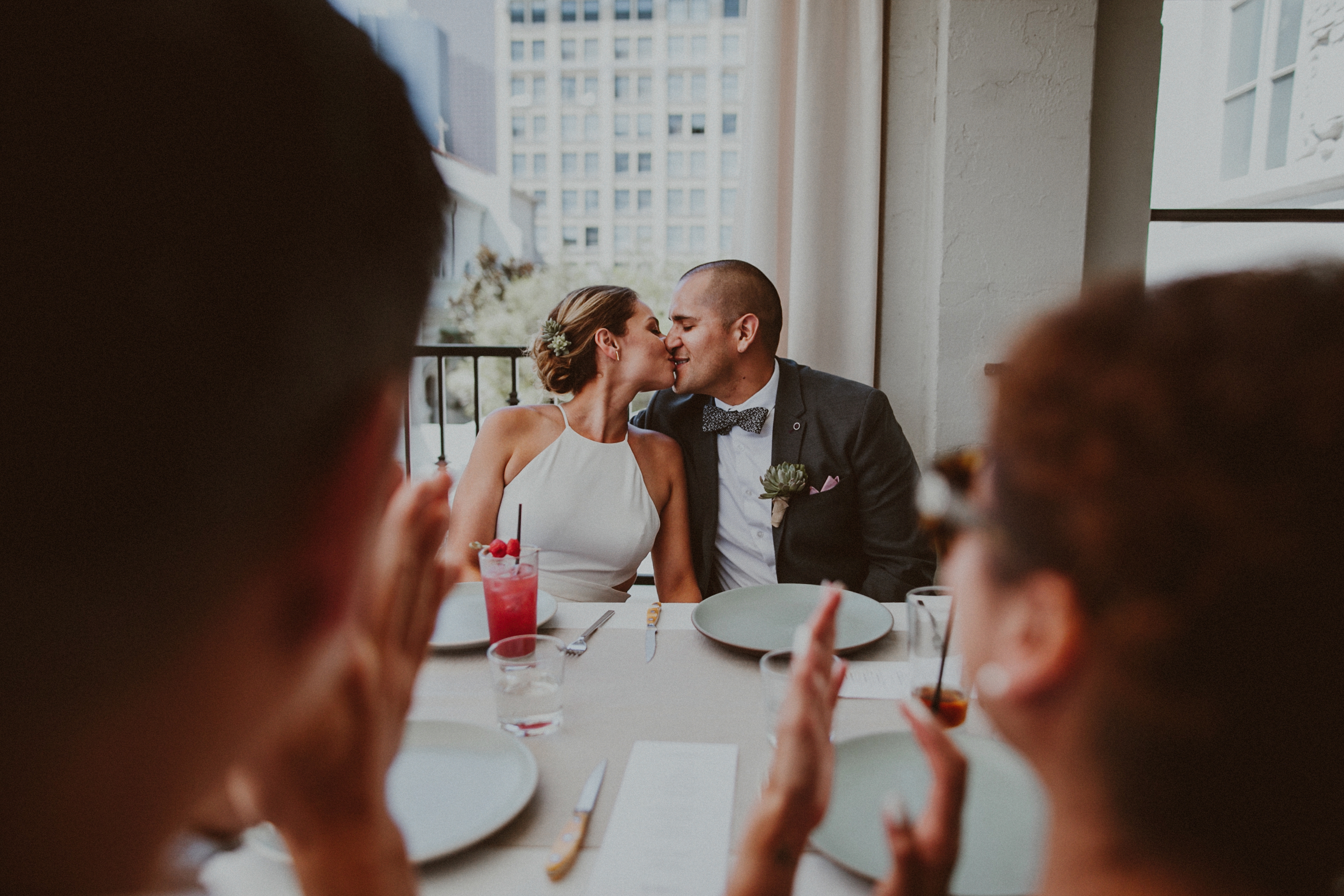 a bride and groom seated at outdoor table and kissing