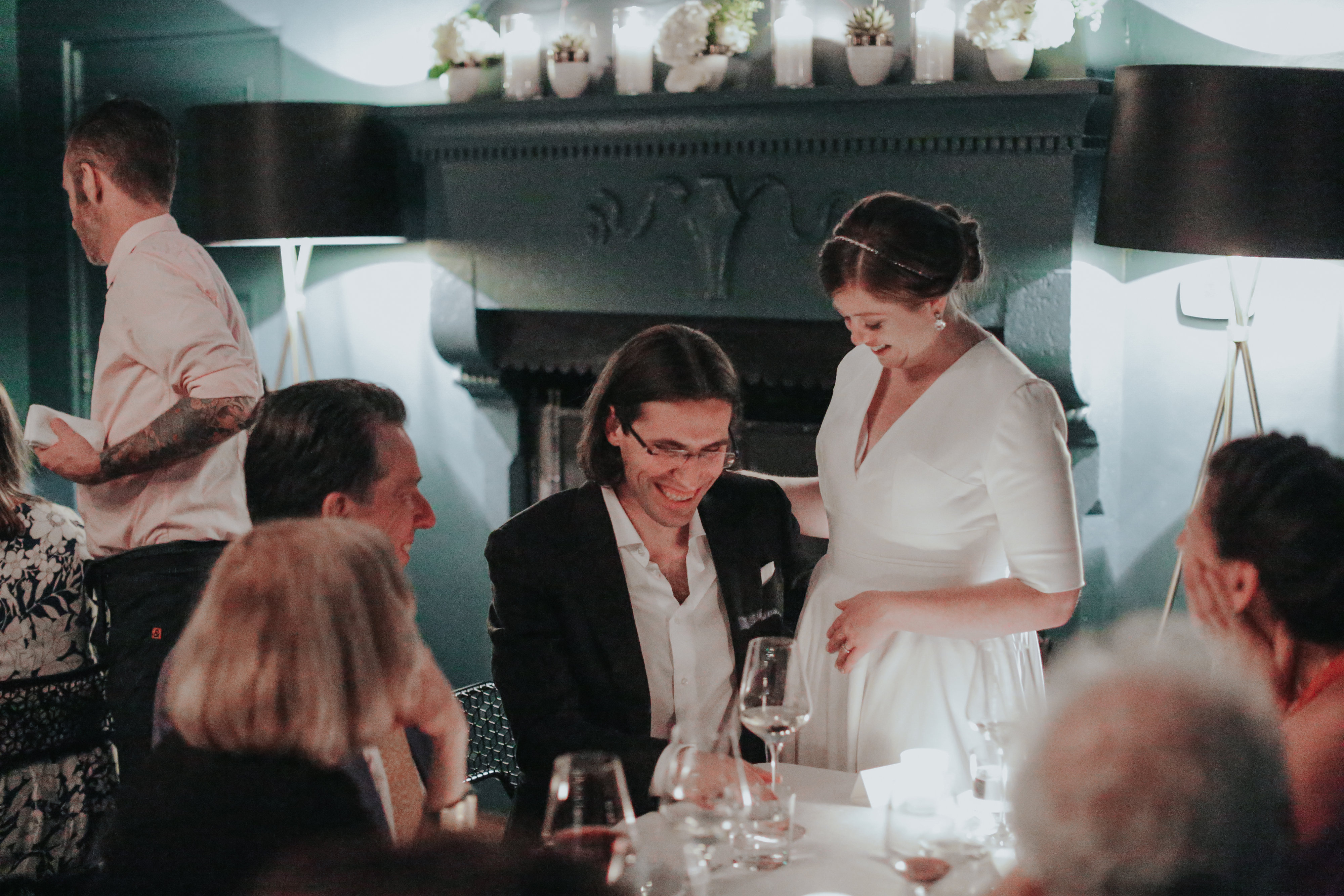 A bride and groom laughing together at a private discussion held among friends at a dinner table