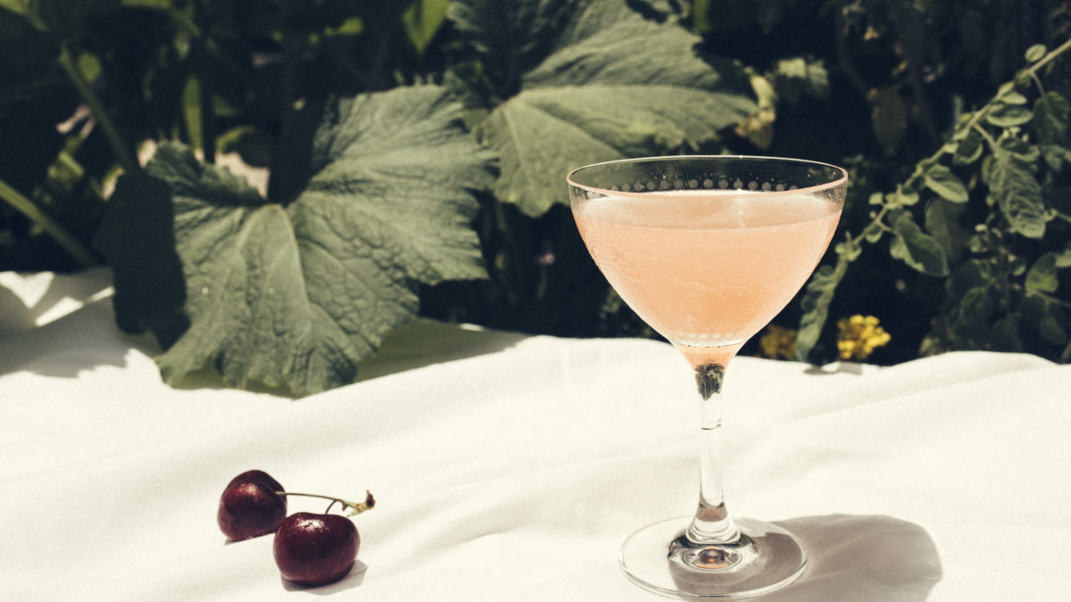 pink cocktail on an outdoor table next to cherries