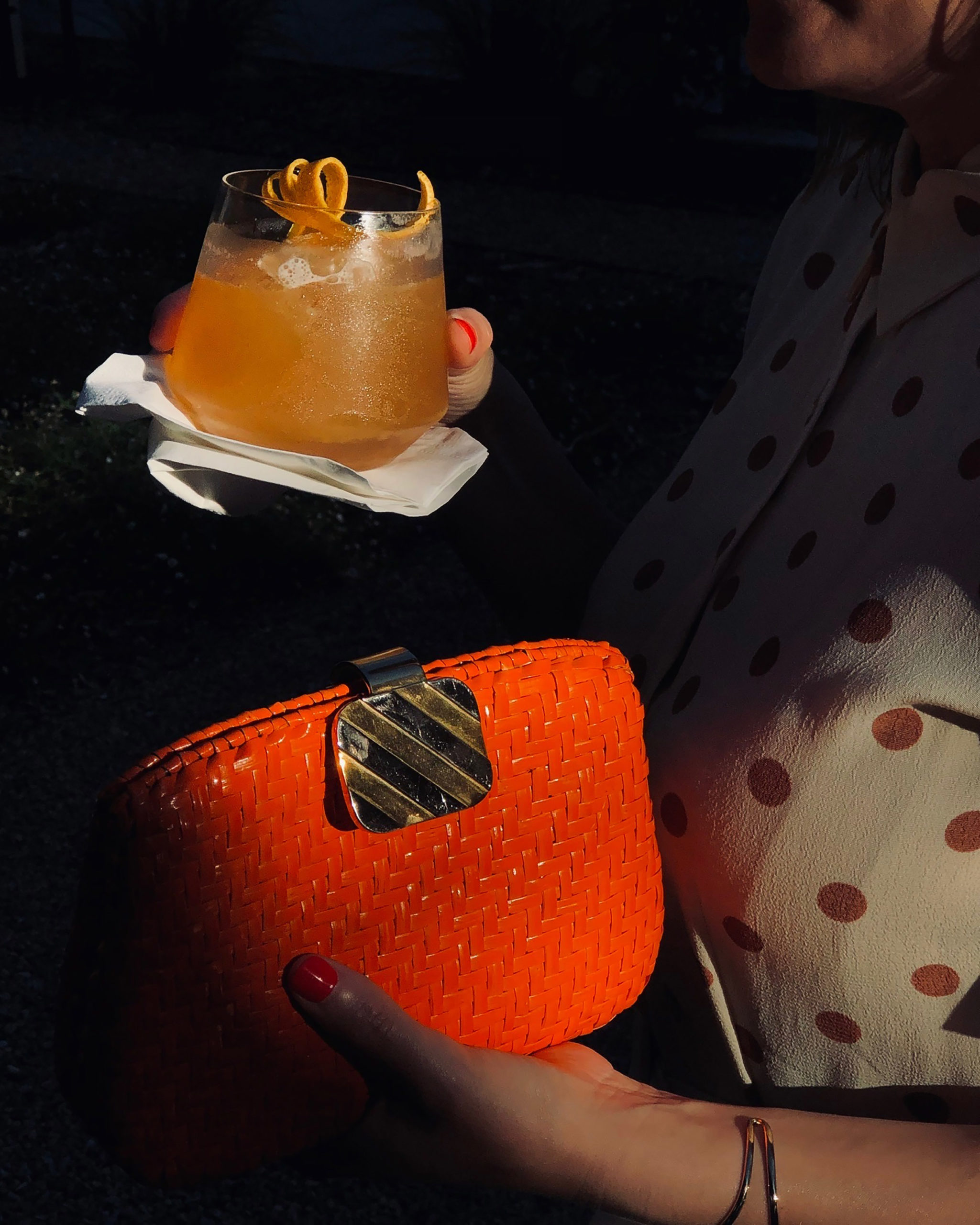 woman holding an orange cocktail with Orange purse