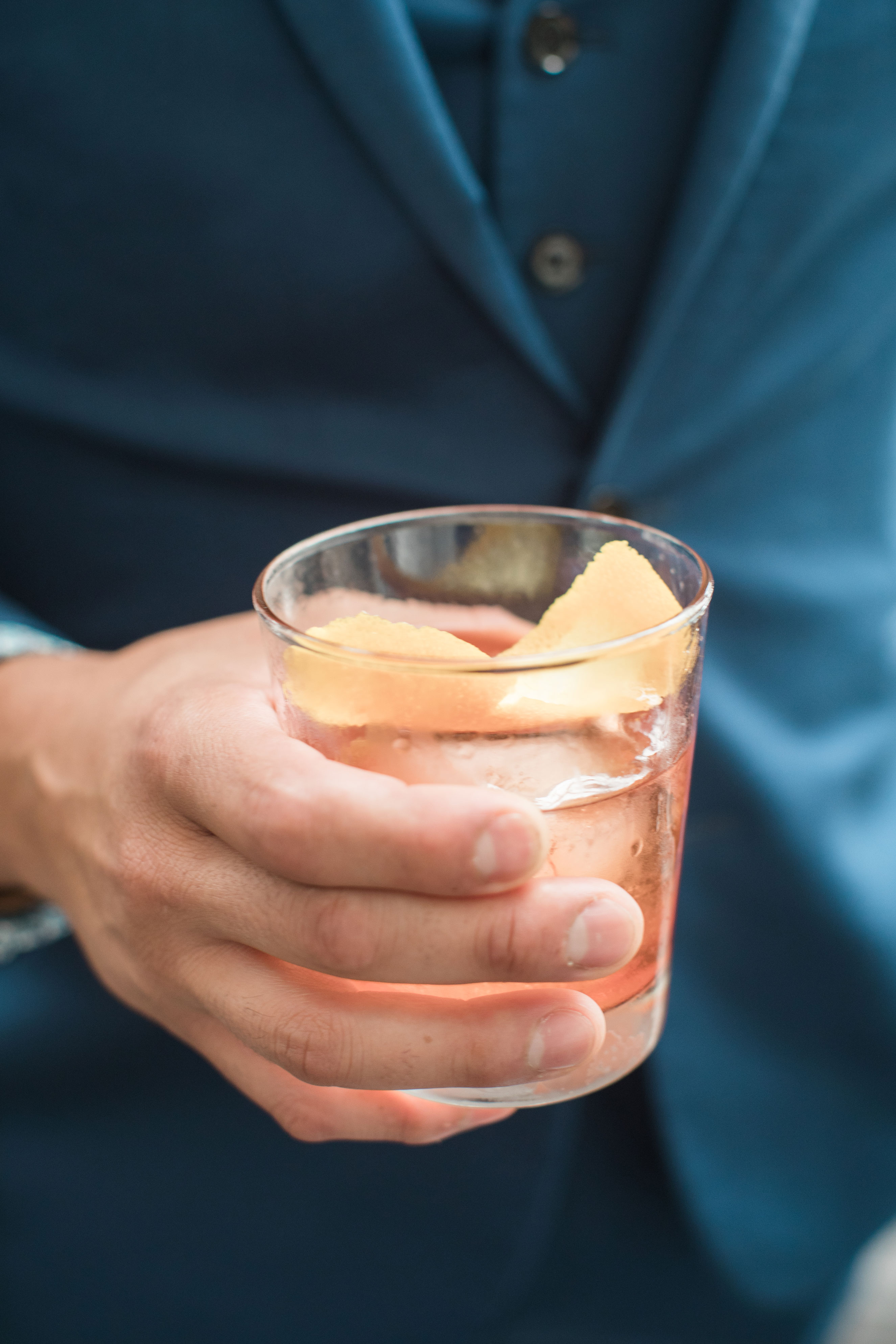 man in suit holding a cocktail with an orange rind