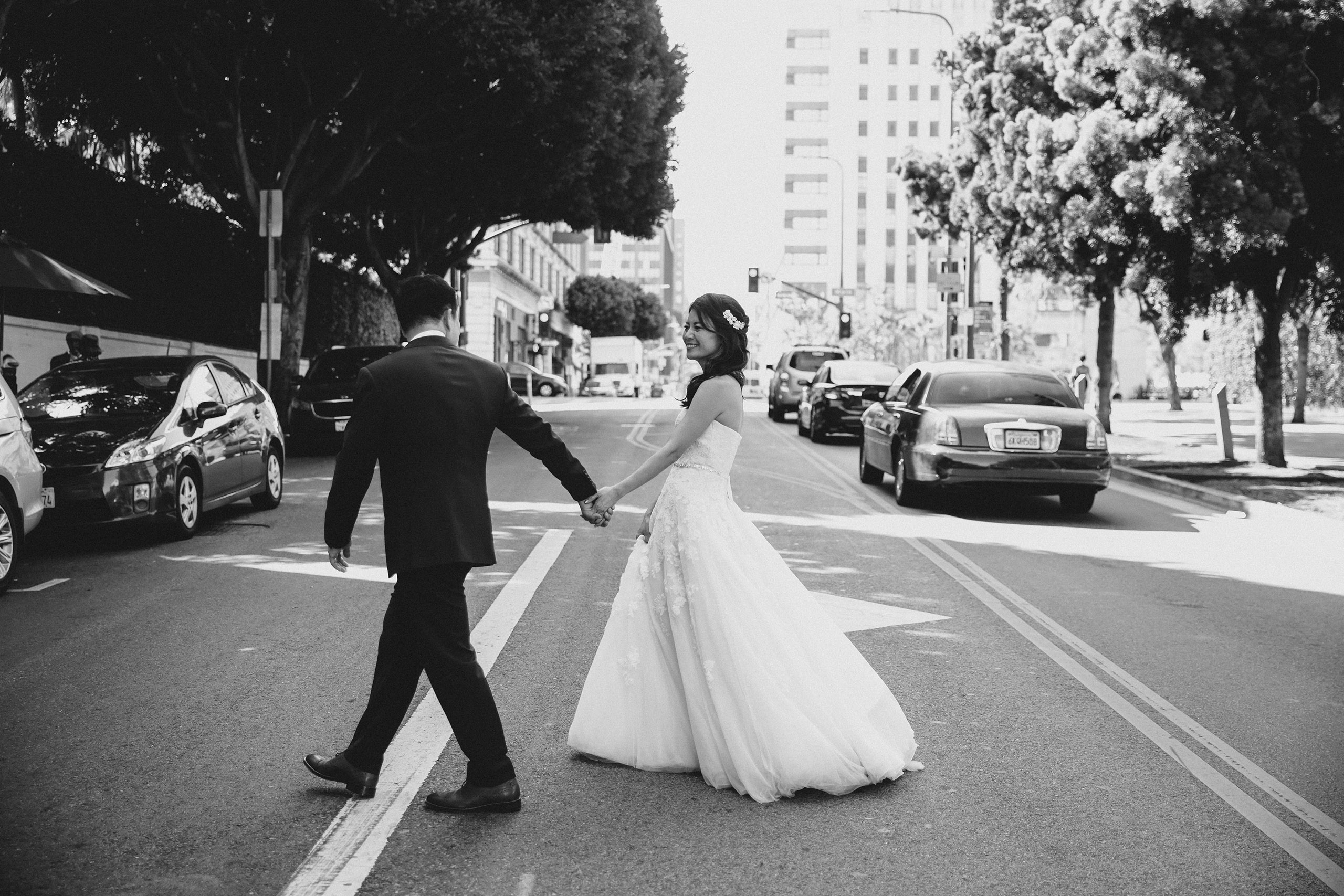 black and white photo of bride and groom walking across street traffic