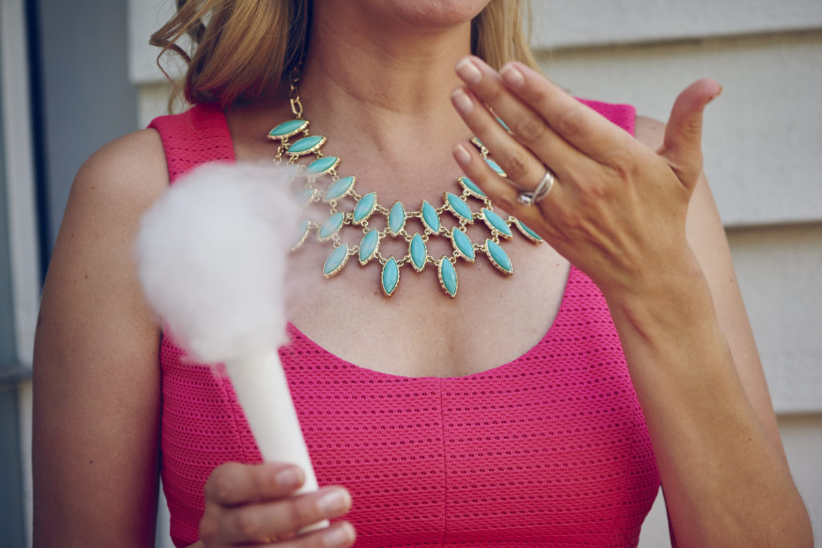 woman wearing pink dress and green cocktail necklace while holding a small cone of cotton candy