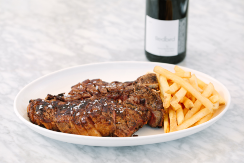 plate of steak and french fries on marble table with a bottle of red wine